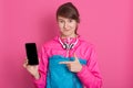 Pretty smiling Caucasian woman in blue and rose sport shirt showing blank smartphone screen and pointing her finger at phone, Royalty Free Stock Photo