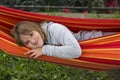 Pretty smiling fair little girl in grey sweater looking out from a colourful hammock