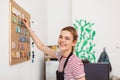 Pretty smiling girl in black apron standing near colorful materials board happily looking in camera at modern pottery