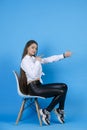 Pretty, smiling girl pointing, with outstretched hand, while sitting in chair and looking at camera. Royalty Free Stock Photo