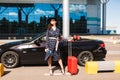 Pretty smiling girl in sunglasses and black hat holding on heels passport with flight ticket and red suitcase near Royalty Free Stock Photo