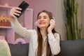 Beautiful woman listening to music at home. Pretty smiling girl taking selfie on smartphone, listening to music, sitting Royalty Free Stock Photo