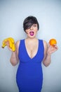 Cute chubby girl with short black hair in a blue dress holding an orange and bananas in her hands, smiling with love for fruits on