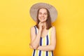 Pretty smiling happy woman wearing striped swimming suit and hat isolated on yellow background keeps hands under chin looking at Royalty Free Stock Photo