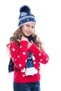 Pretty smiling little girl with curly hairstyle wearing knitted sweater, scarf and hat with skates isolated on white background. Royalty Free Stock Photo