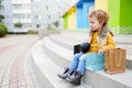 Pretty smiling little girl with shopping bags sitting near shopping center Royalty Free Stock Photo