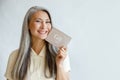 Pretty smiling mature Asian lady holds gift card on light grey background in studio