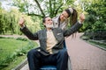 Pretty smiling modern granddaughter, nurse, or care giver walking in the park with senior disabled man in wheelchair Royalty Free Stock Photo