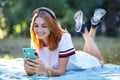 Pretty smiling teenage girl listening to music in pink earphones and using sellphone outdoors Royalty Free Stock Photo