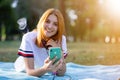Pretty smiling teenage girl with red hair using sellphone outdoors in park Royalty Free Stock Photo
