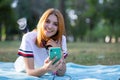 Pretty smiling teenage girl with red hair using sellphone outdoors in park Royalty Free Stock Photo
