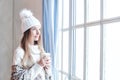 Pretty smiling winter woman holding hot dring and resting at home, romantic portrait