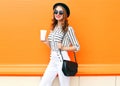Pretty smiling woman with coffee cup wearing fashion black hat white pants handbag clutch over colorful orange Royalty Free Stock Photo