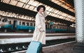 Pretty smiling woman at the railway station. Positive tourist lady in a hat and coat who is standing at the railway station with a