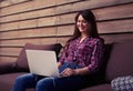 Pretty smiling woman sitting on the sofa with laptop on her knee Royalty Free Stock Photo