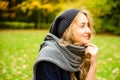 Pretty smiling woman wearing knitting hat and scarf thoughtfully looking side outdoor in the city park in fall season