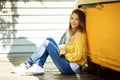 Pretty smiling woman is wearing yellow sweater drinking coffee latte near old retro bus Royalty Free Stock Photo