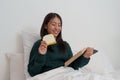 Pretty smiling young asian woman relaxing at home on bed and reading book. Lifestyle concept Royalty Free Stock Photo