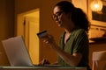 Pretty smiling young Caucasian woman wearing is sitting at table, using laptop and holding bank credit card. Concept of Royalty Free Stock Photo