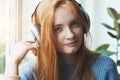 smiling young red haired girl with headphones listening to music at home, relaxing, enjoying songs Royalty Free Stock Photo