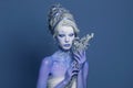 Pretty Snow Queen or Winter Witch woman with perfect fantasy makeup and painted body on blue background. Carnival and Halloween