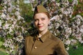 Soviet female soldier in uniform of World War II stands near flowering tree