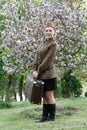Soviet female soldier in uniform of World War II with suitcase stands on a stump near flowering tree Royalty Free Stock Photo