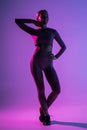 Pretty sporty woman with perfect body standing  on purple light background Royalty Free Stock Photo