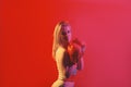 Pretty strong young woman boxer posing isolated over red background wearing boxing gloves.