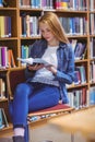 Pretty student sitting on chair reading book in library Royalty Free Stock Photo