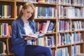 Pretty student sitting on chair reading book in library Royalty Free Stock Photo