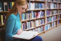 Pretty student sitting on chair reading book in library Royalty Free Stock Photo