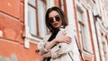 Pretty stylish beautiful young woman with sexy lips in trendy sunglasses in fashionable beige trench coat posing near vintage Royalty Free Stock Photo