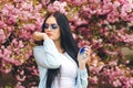 Pretty stylish girl in glasses. Pink sakura flower bloom in spring. Perfume, cosmetics concept. Beautiful woman applying perfume