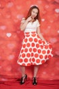 Pretty stylish pin up girl in white shirt and red polka dot vintage skirt standing on red hearts background Royalty Free Stock Photo