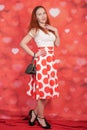 Pretty stylish pin up girl in white shirt and red polka dot vintage skirt standing on red hearts background Royalty Free Stock Photo