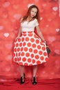 Pretty stylish pin up girl in white shirt and red polka dot vintage skirt standing on red hearts background Royalty Free Stock Photo