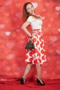 Pretty stylish pin up girl in white shirt and red polka dot vintage skirt standing on red hearts background Royalty Free Stock Photo