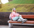 Pretty stylish smiling roller girl on the bench in the city park