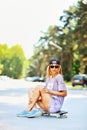 Pretty stylish woman sitting on skateboard