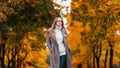 Pretty stylish young hipster woman in a fashionable knitted sweater in an elegant long coat in jeans with glasses walks through an Royalty Free Stock Photo