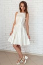 Pretty sweet pretty girl in a white dress in bright fashion shoes near a brick wall in the studio