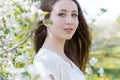 Pretty sweet tender young girl with a bright smile with long blond hair among the blossoming apple trees