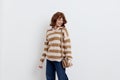 a pretty sweet woman is standing on a light background in a striped sweater and a bag on her shoulder, standing straight Royalty Free Stock Photo