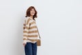 a pretty sweet woman is standing on a light background in a striped sweater and a bag on her shoulder, standing straight Royalty Free Stock Photo
