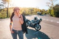 Pretty tattoed girl with a leather jacket poses against the background of a motorcycle by the road. Motorcycle local Royalty Free Stock Photo