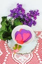 Pretty tea or coffee cup with silver trim filled with pink and purple paper hearts sitting on a white heart doily with a pink rose