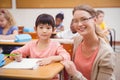 Pretty teacher helping pupil in classroom smiling at camera