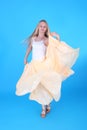 Pretty teenage blond girl dancing in the yellow dress, blue background Royalty Free Stock Photo