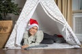 A pretty teenage boy in a Santa hat lying in a children& x27;s tent in a room waiting impatiently for Santa.